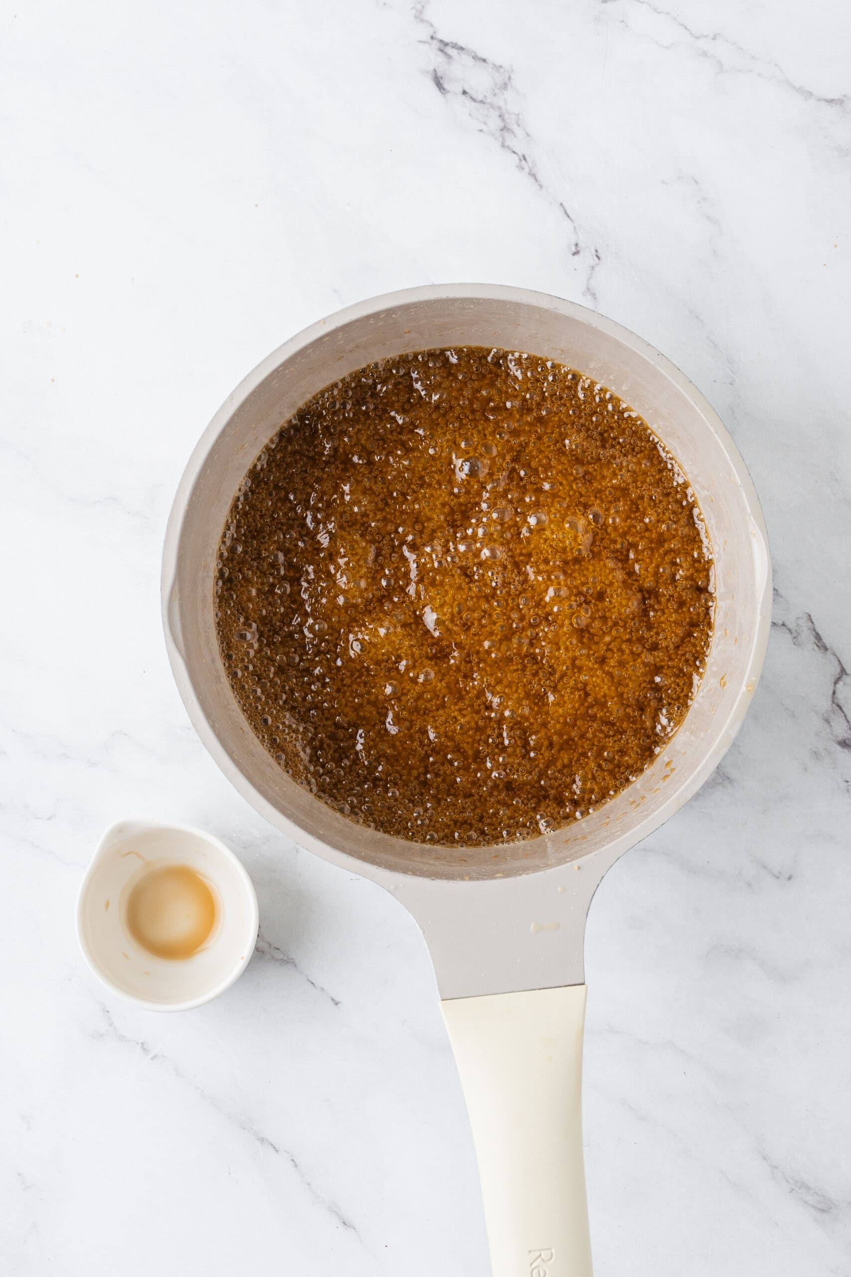 Golden-brown sugar mixture bubbling in a saucepan with a small bowl of vanilla extract beside it.