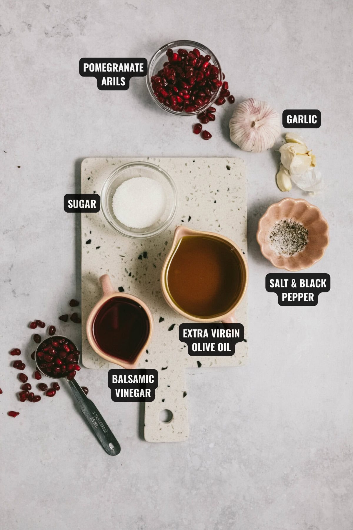 ingredients for pomegranate salad dressing recipe including pomegranate arils, garlic, sugar, balsamic vinegar, extra virgin olive oil, salt, and black pepper